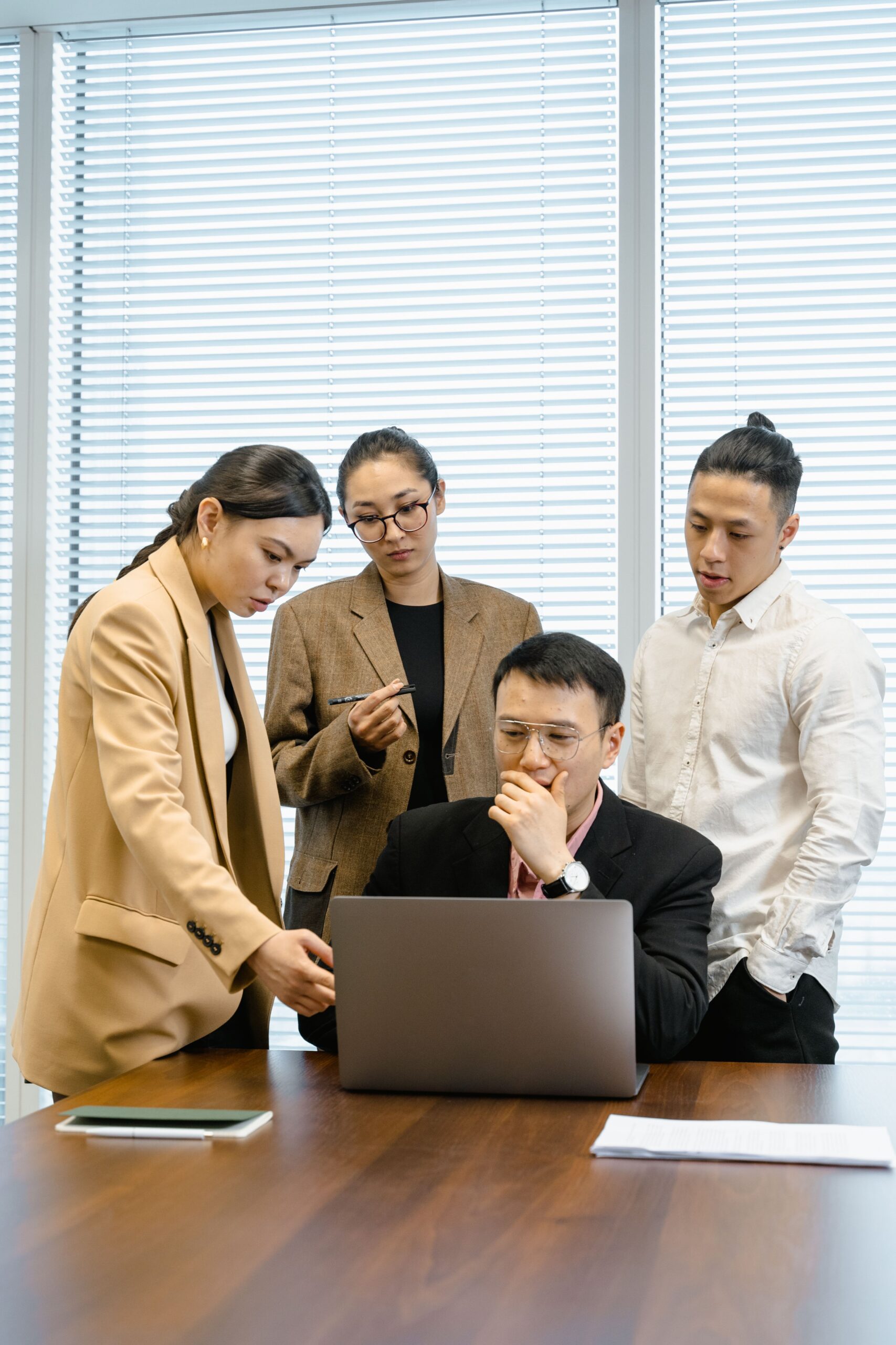 A group of colleagues engaged in a meeting, discussing around a laptop in a modern office.